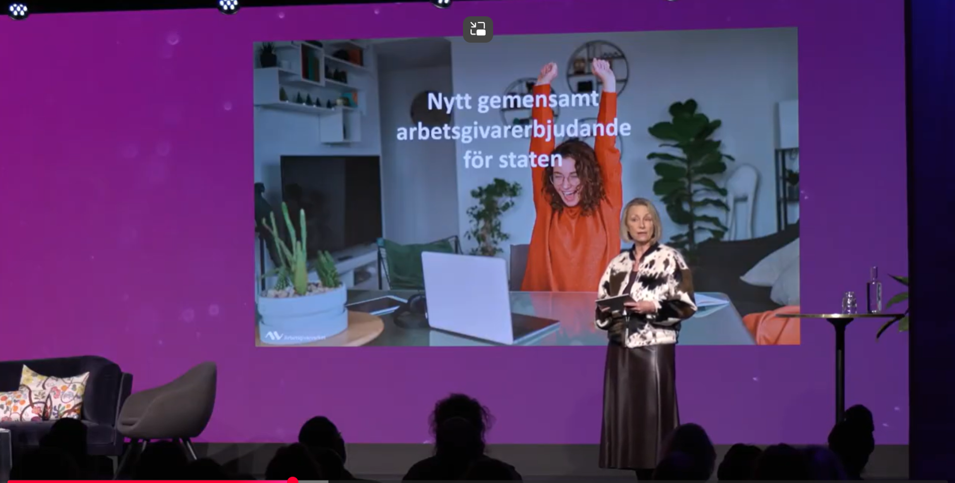 Ann Follin talar framför stor skärm på en scen.